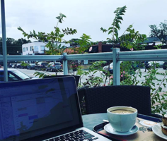 laptop at a cafe table with a beautiful view, sitting next to a latte